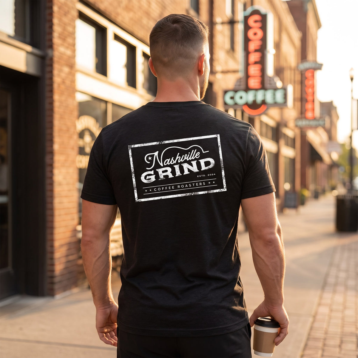 Back of the Nashville Grind Logo Tee showing the large Nashville Grind Coffee Roasters stamp logo, worn on a Nashville street