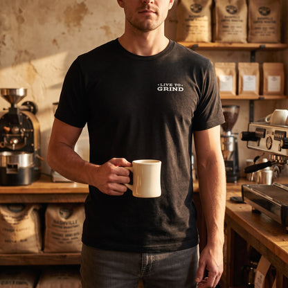 Man wearing the Nashville Grind Logo Tee in black heather with the Live to Grind chest print, holding a coffee mug in a Nashville coffee roastery