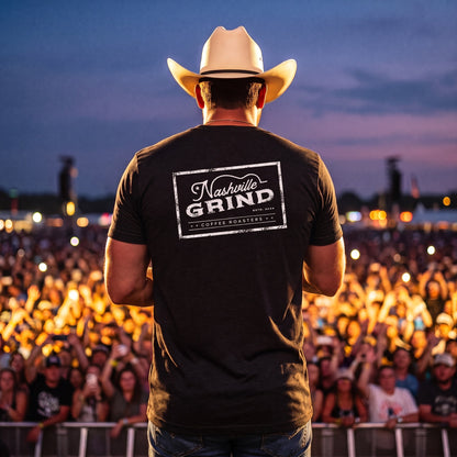 Country performer in a cowboy hat wearing the Nashville Grind Logo Tee on a festival stage, back logo facing the crowd
