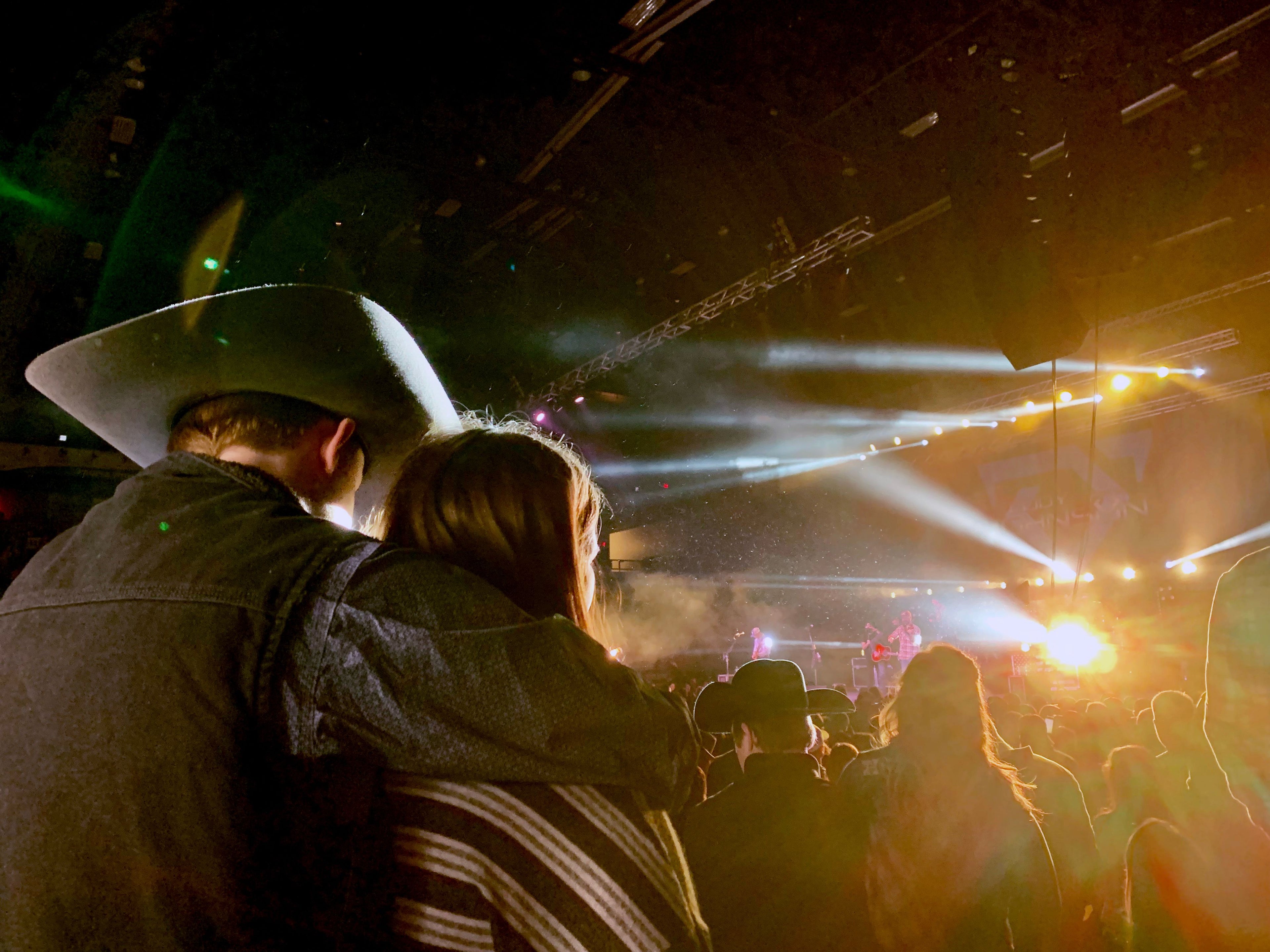 Country music fans in cowboy hats watching a concert with stage lights